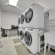 Modern laundry room with stacked washers and dryers, utility sink, storage shelves, and detergent supplies.